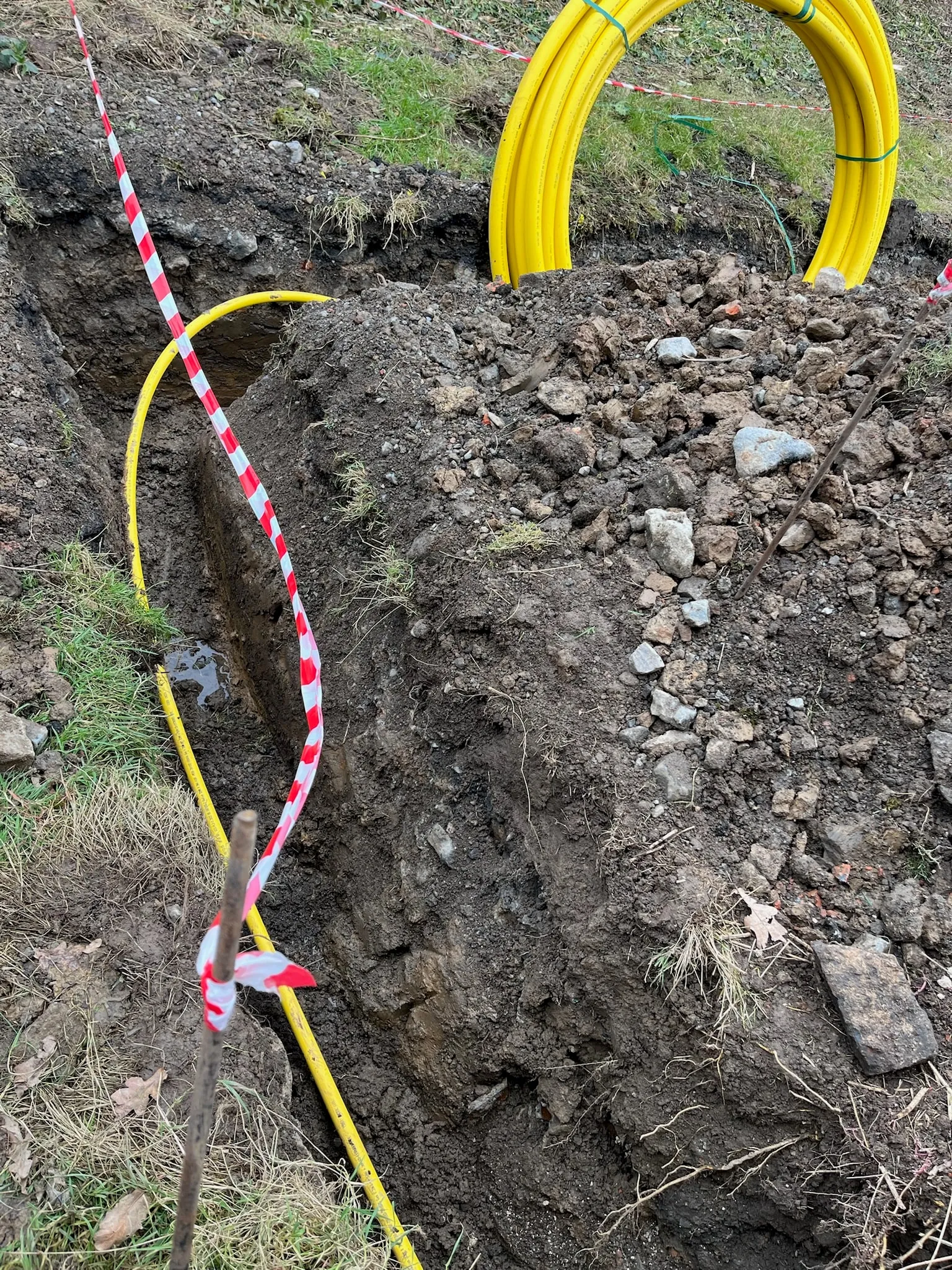 A freshly dug trench with a yellow gas pipe running along it and a coil of pipe beside it